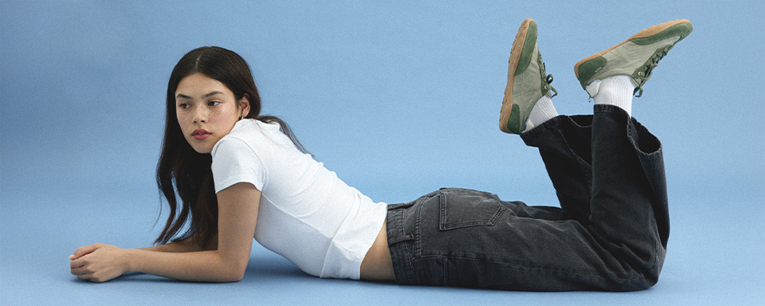 Person lying on a blue background wearing a white shirt, black pants, and green shoes.